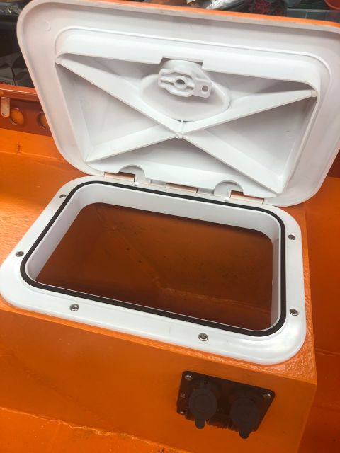 1992 Jeep Wrangler - A white hatch is open on the orange interior of a boat, revealing a dark, liquid-filled compartment below.