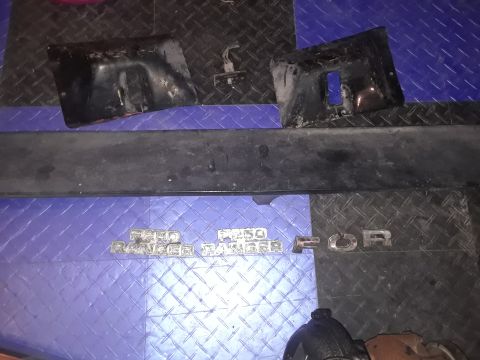 1994 Ford Bronco - Emblems and bumper components are laid out on a textured blue surface.
