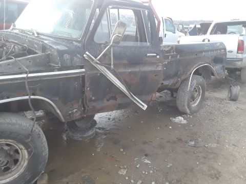 1994 Ford Bronco - This heavily rusted black pickup truck, likely a 1979 Ford F-Series, sits in a junkyard with several other vehicles visible.