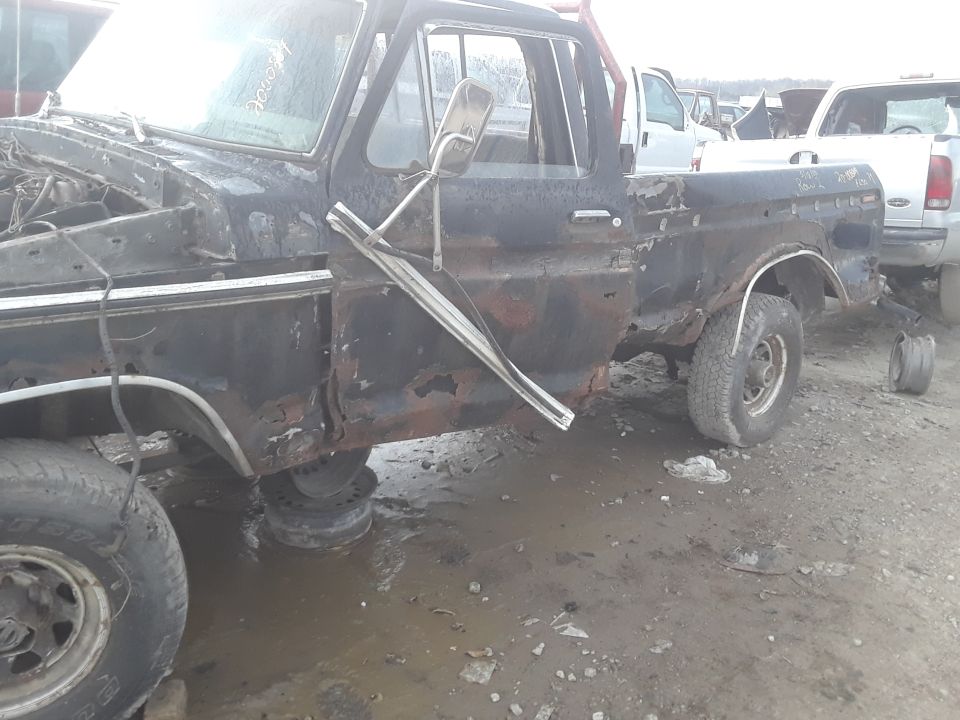 Side view of a rusty black 1979 Ford F-Series pickup truck with missing parts