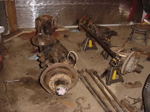 1992 Ford Bronco - Several vehicle axle assemblies and driveshafts are laid out on the floor of a garage.