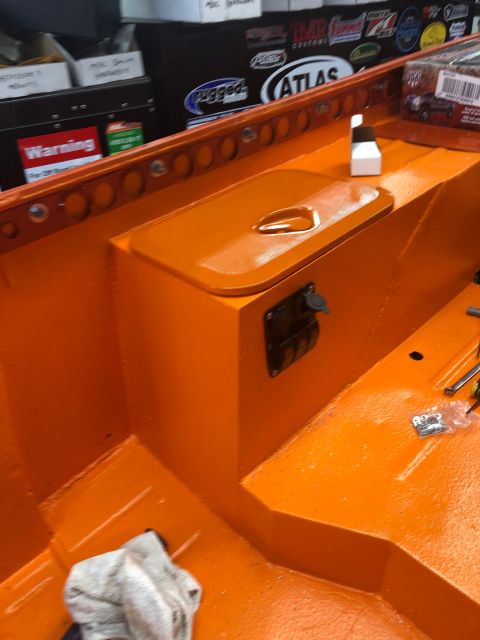 1992 Jeep Wrangler - Freshly orange-painted truck bed interior showing a wheel-well storage box with latch and outlet, plus stake-pocket holes and decals.