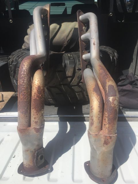 1979 Ford Bronco - Two rusty exhaust headers are laid out on a surface, possibly a truck bed.
