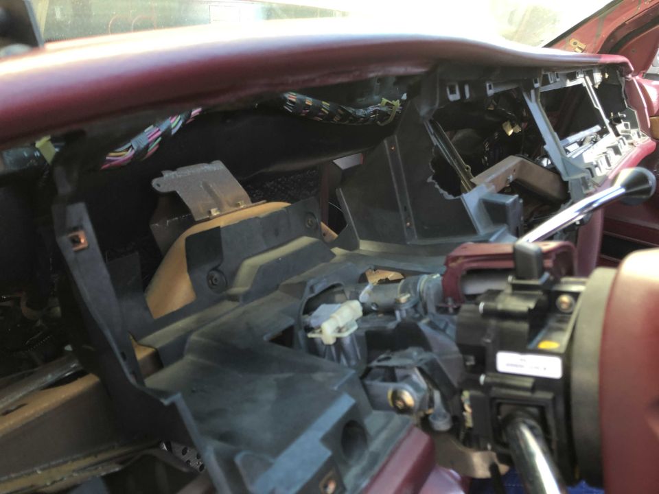 Disassembled dashboard of a car, showing wiring and internal components. Steering column visible