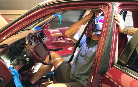 1992 Ford Crown Victoria - A person wearing a welding mask works on the interior of a car, with the door open and dashboard partially disassembled.