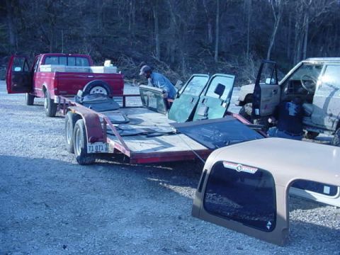 1992 Ford Bronco - A red pickup truck tows a trailer loaded with Jeep doors and a hardtop, with another Jeep visible in the background.