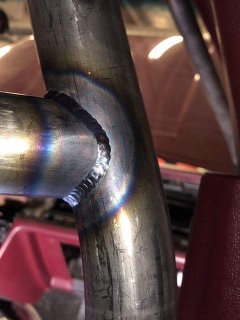 1992 Ford Crown Victoria - A close-up view of a welded metal tube joint, with a hint of a red vehicle interior in the background.