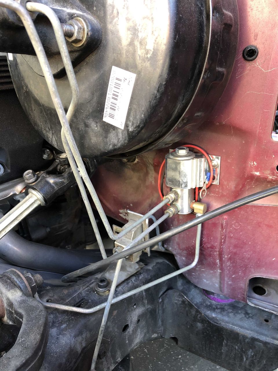Close-up of brake booster, vacuum lines, and solenoid valve. Sticker on booster has barcode