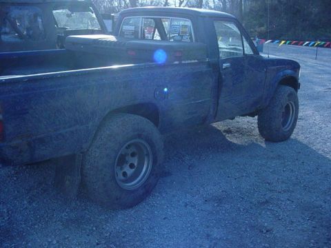 1992 Ford Bronco - Side view of a dark blue pickup truck, possibly from the early 1980s, with another vehicle in the background.