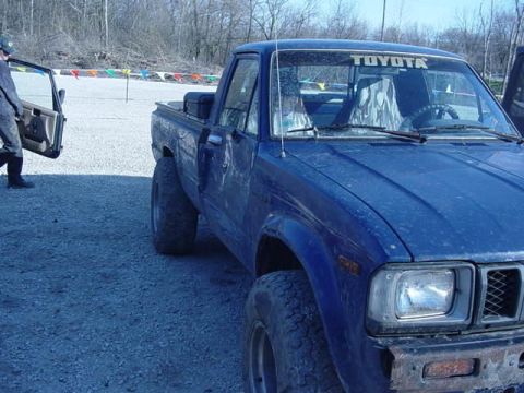 1992 Ford Bronco - A blue Toyota pickup truck is parked on a gravel lot with the driver's door ajar.