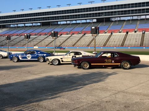 1970 Ford Mustang - Several vintage race cars are lined up on the track, with grandstands in the background.
