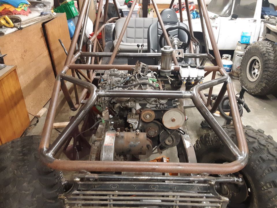 Custom buggy frame with exposed engine, seats, and steering wheel. Large tires visible