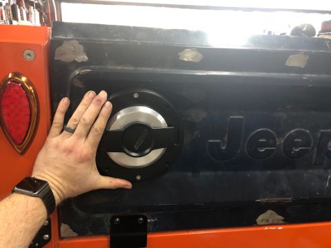 1992 Jeep Wrangler - A hand is shown covering a black fuel filler cap installed on the rear panel of a Jeep.