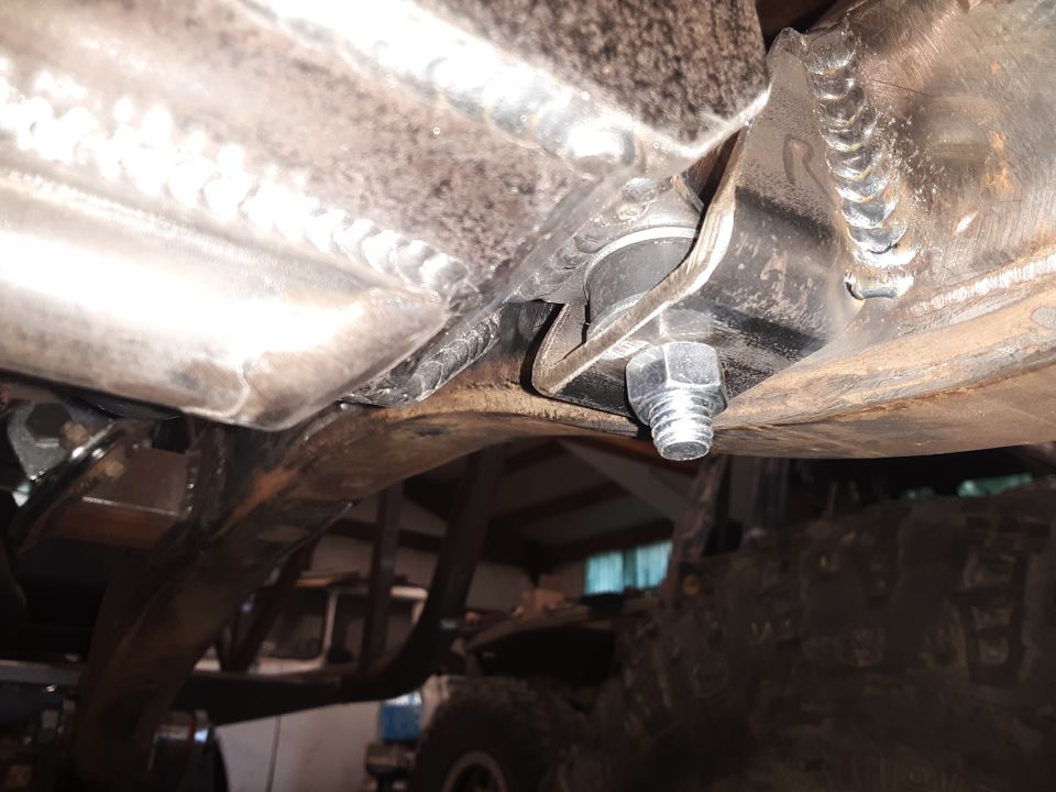 Undercarriage view of a vehicle's suspension with a prominent bolt and welded metal