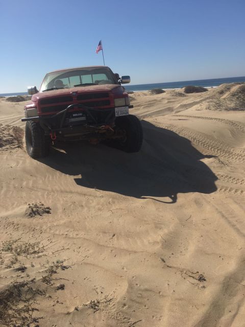 1996 Dodge 1500 - Red Dodge 1500 pickup truck with winch and American flag on antenna, driving on sand dunes near the ocean.