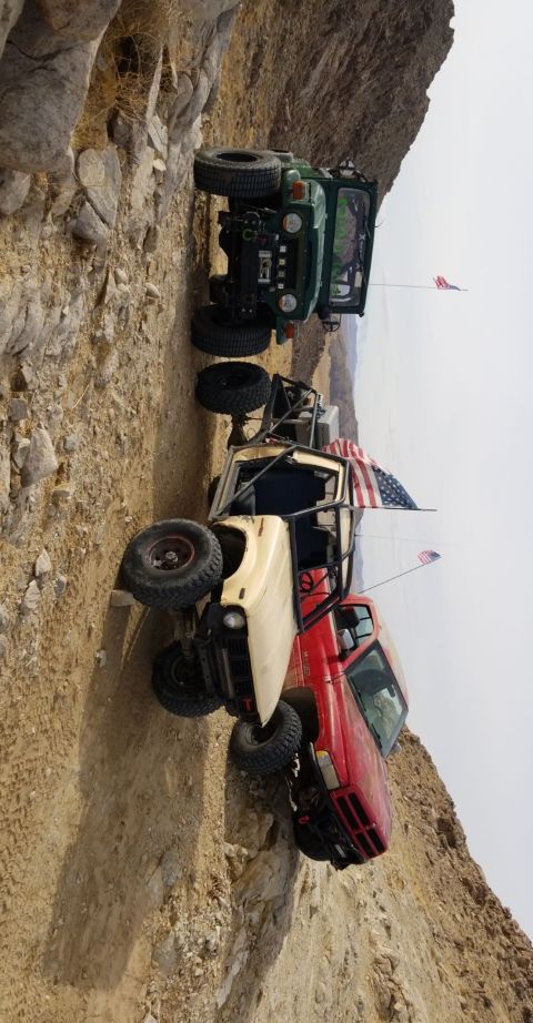 1996 Dodge 1500 - Multiple off-road vehicles navigate a challenging rocky terrain on an incline, with American flags attached to some.