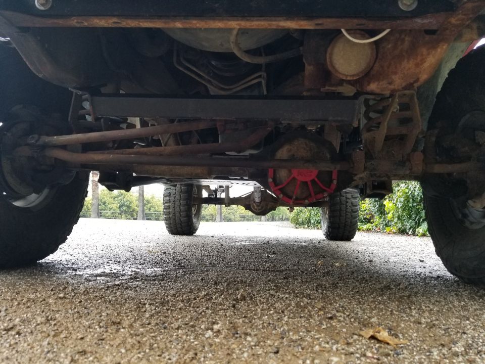 Underside view of a truck's drivetrain and suspension components. Shows the rear differential with a red cover