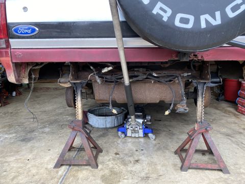 1994 Ford Bronco - The rear of a Ford Bronco is elevated on jack stands, revealing its undercarriage and wiring during a rebuild.