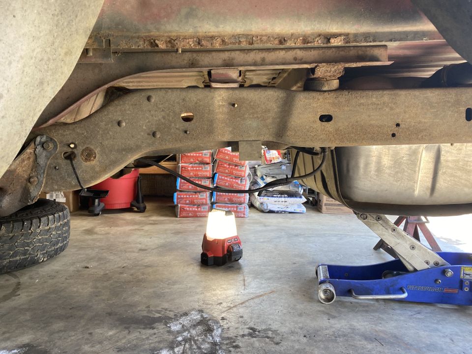 underbody of a truck with a fuel tank and frame visible, being worked on with a jack