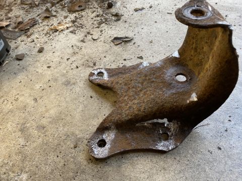 1994 Ford Bronco - A heavily rusted metal bracket with several mounting holes is shown on a concrete surface.