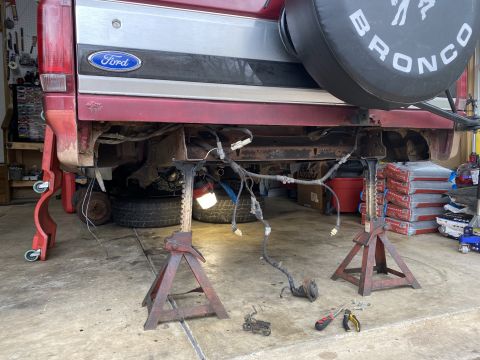 1994 Ford Bronco - The rear of a Ford Bronco is shown on jack stands, with its wiring harness exposed for repair.