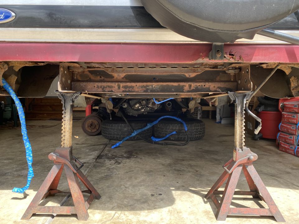 Vehicle undercarriage on jack stands, showing rusty frame and suspension components