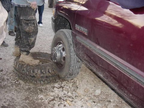 1992 Ford Bronco - A person stands on a flat tire next to a maroon truck with RAM 3500 badging.