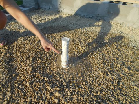 1992 Ford Bronco - A hand points to a white pipe protruding from a gravel surface, with a concrete structure visible behind it.