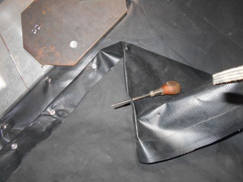 1992 Ford Bronco - A screwdriver is used to help secure a piece of black textured material with rivets.