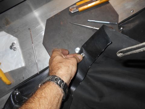 1992 Ford Bronco - A hand is shown attaching a grommet to a piece of black fabric, with tools visible in the background.