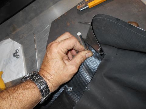 1992 Ford Bronco - Close-up of a hand wearing a watch as it punches a hole in black material with a metal edge.