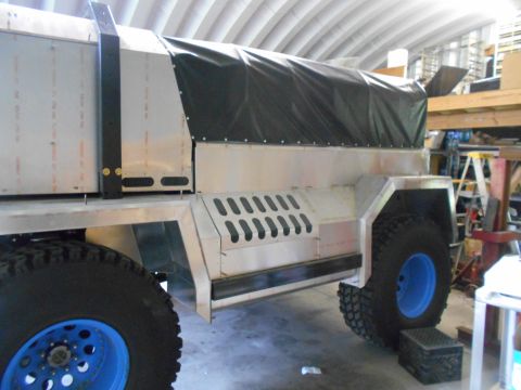 1992 Ford Bronco - This custom truck bed, covered by a black tarp, has large off-road tires with distinctive blue rims.
