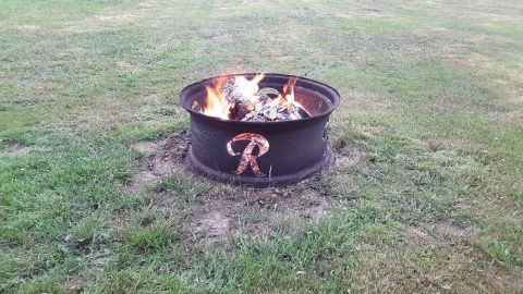 1985 Toyota Hilux - A fire pit constructed from a tire rim burns brightly in a grassy outdoor setting.