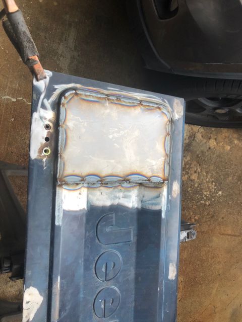 1992 Jeep Wrangler - A Jeep tailgate shows a freshly welded patch, indicating body repair work is underway.