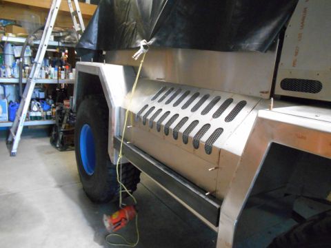 1992 Ford Bronco - Side view of a custom vehicle build, a unique metal panel with ventilation cutouts and a bright blue wheel rim.