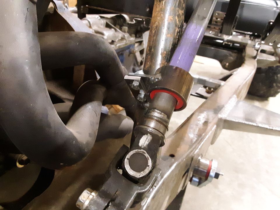 Close-up of vehicle frame with exhaust pipes and a purple-colored shaft with red bushings