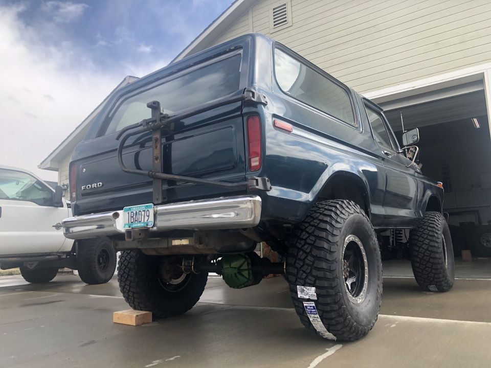 Dark green 1978 Ford Bronco with large tires, rear view, mounted spare tire carrier, and chrome bumper