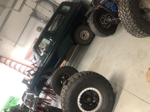 1979 Ford Bronco - A dark green SUV is elevated on stands, surrounded by large off-road tires in a garage setting.