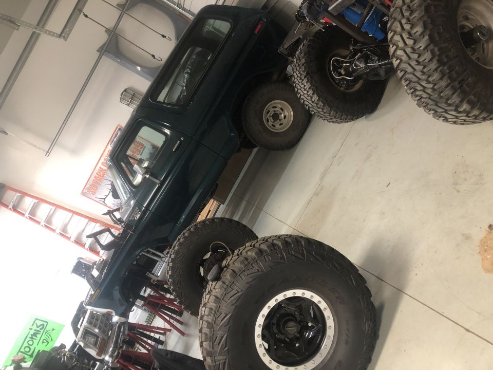 dark green SUV on stands with large off-road tires around it