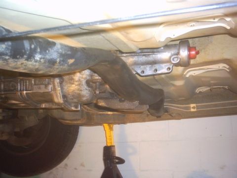 1991 Ford LTD Crown Victoria - The underside of a vehicle is visible, with focus on the transmission and exhaust system, supported by a jack stand.