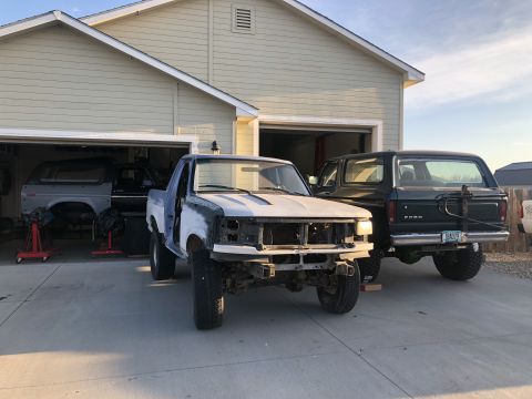 1979 Ford Bronco - A 1978 Ford Bronco is parked next to a pickup truck undergoing repairs in front of a garage.