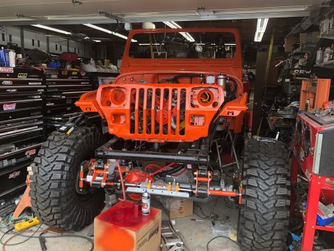1992 Jeep Wrangler - This orange Jeep Wrangler is undergoing modifications in a garage, a lifted suspension and oversized tires.