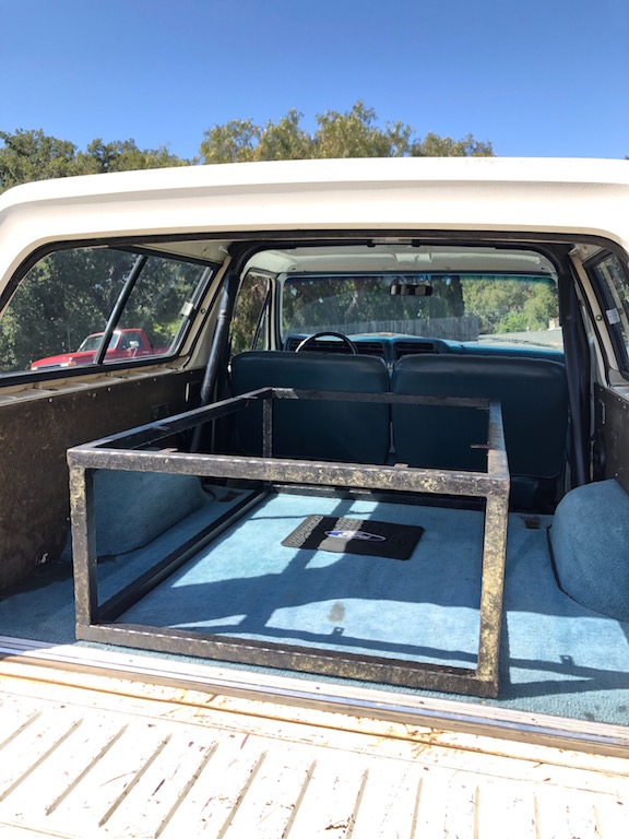 White 1978 Ford Bronco interior, rear view, with blue carpet and a metal frame in the cargo area