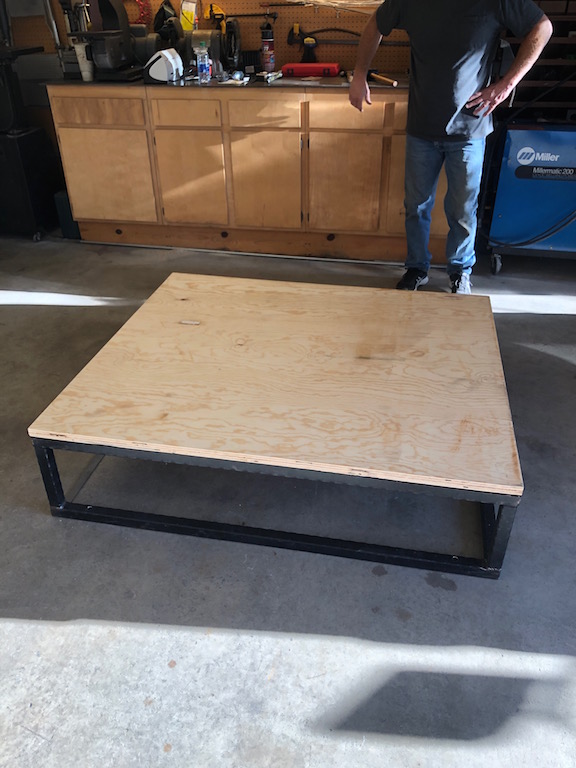 Plywood platform on a black metal frame in a garage setting