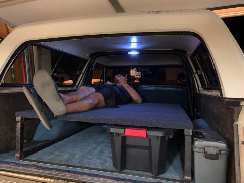 1981 Ford Bronco - A person relaxes inside the converted interior of a 1981 Ford Bronco, set up with a sleeping platform and storage.