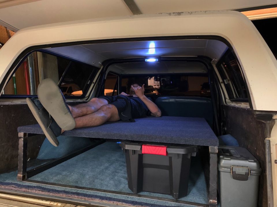 Interior of a 1981 Ford Bronco with a bed platform and a person resting