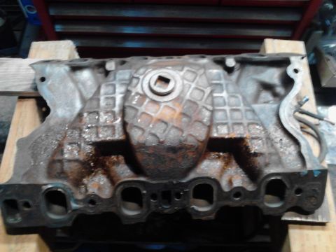 1978 Ford Bronco - A cast iron engine intake manifold is shown, resting on wooden blocks in what appears to be a workshop.