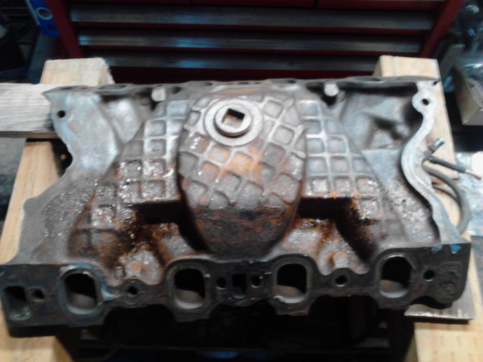 Cast iron engine intake manifold with a square opening in the center, resting on wooden blocks