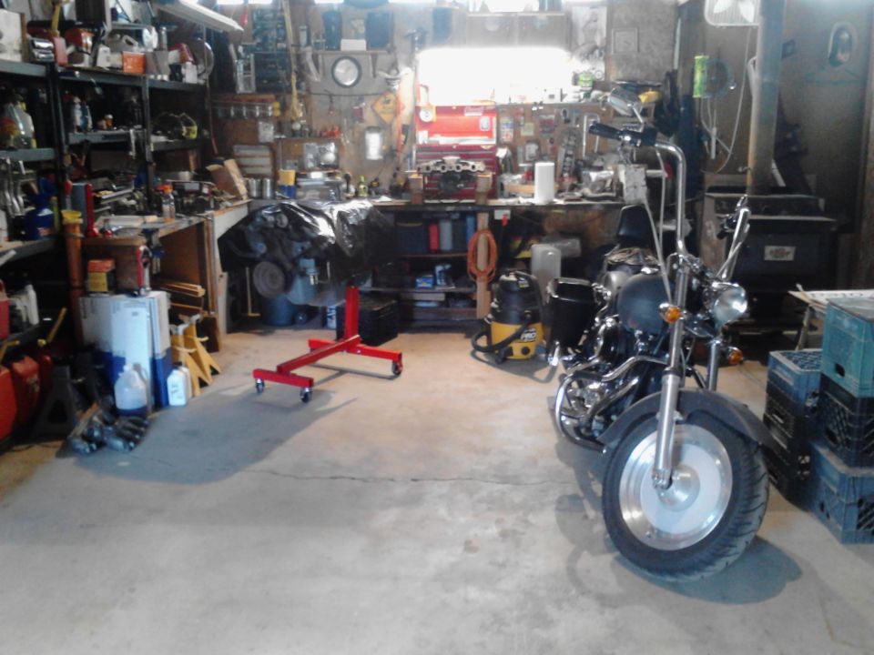 Motorcycle parked in a cluttered garage with tools and engine parts around