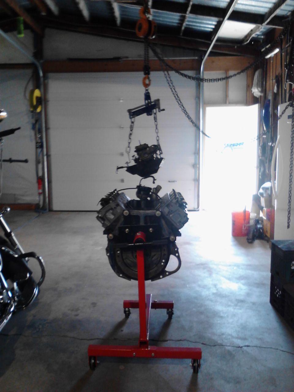 Engine assembly suspended from a hoist and resting on a red engine stand in a garage